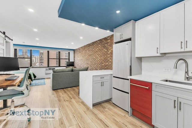235 E 57th St Unit 17A, New York City, NY 10022 - kitchen featuring a sink, light countertops, freestanding refrigerator, white cabinetry, and light wood-style floors