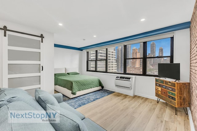 bedroom with a barn door, light wood-type flooring, and a wall unit AC