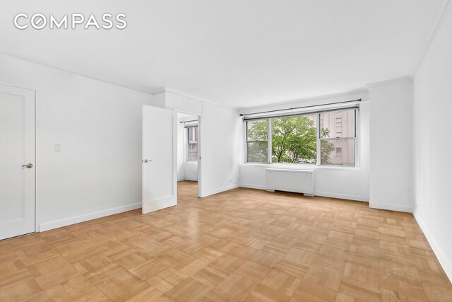 empty room with crown molding, radiator, and light parquet floors