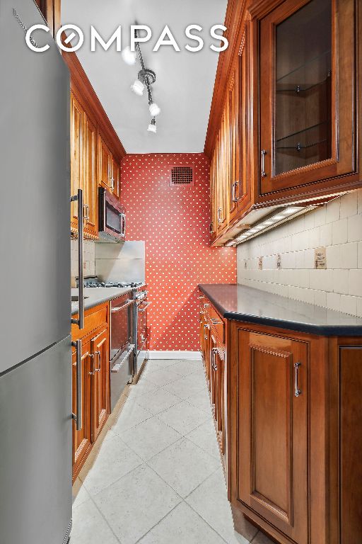 kitchen with wallpapered walls, baseboards, brown cabinetry, dark countertops, and stainless steel appliances