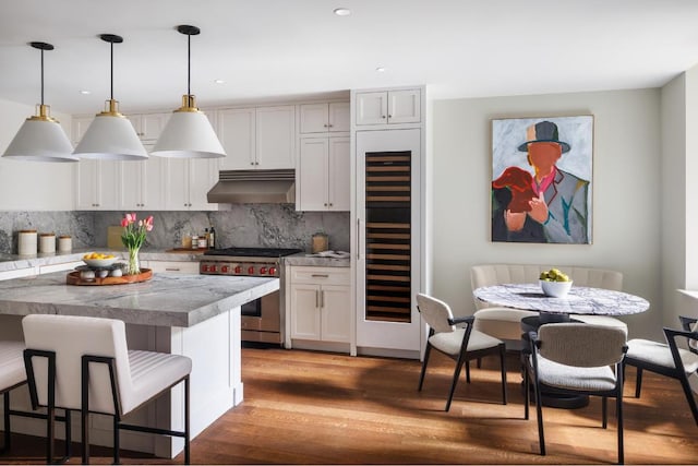 kitchen with hanging light fixtures, under cabinet range hood, high end range, and light countertops