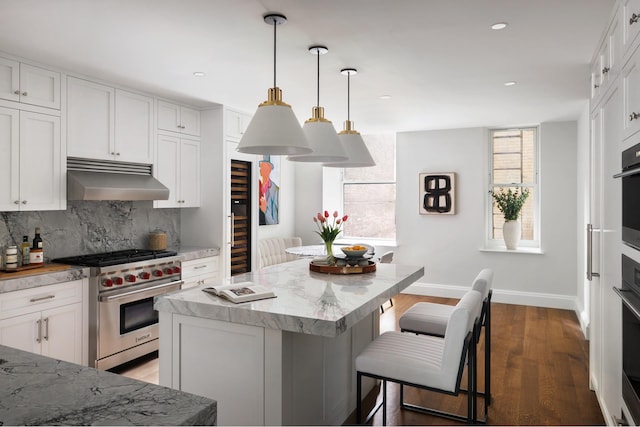 kitchen with light stone counters, under cabinet range hood, light wood-style floors, luxury range, and decorative backsplash