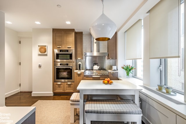 kitchen featuring decorative backsplash, brown cabinetry, appliances with stainless steel finishes, light countertops, and wall chimney range hood