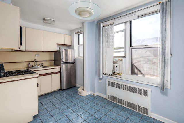 kitchen with baseboards, radiator, freestanding refrigerator, light countertops, and a sink