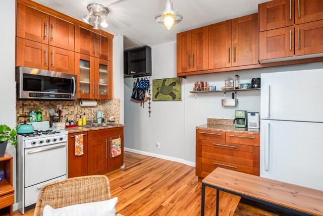 kitchen with light stone counters, white appliances, backsplash, brown cabinets, and glass insert cabinets