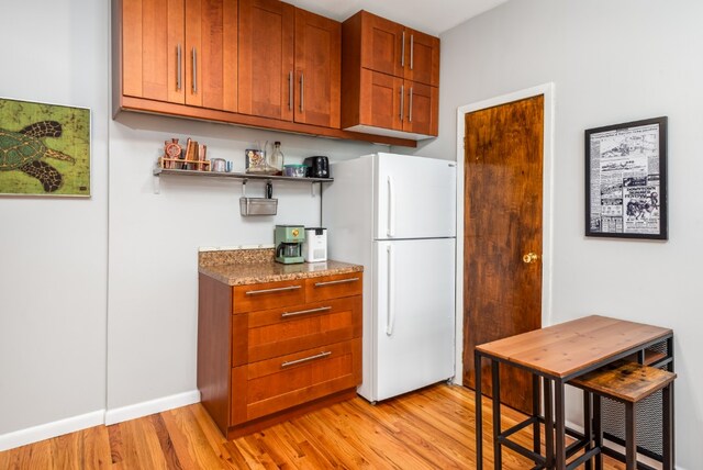 kitchen featuring light wood-style floors, freestanding refrigerator, brown cabinetry, and open shelves