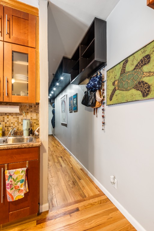 kitchen with light wood finished floors, tasteful backsplash, brown cabinetry, a sink, and baseboards