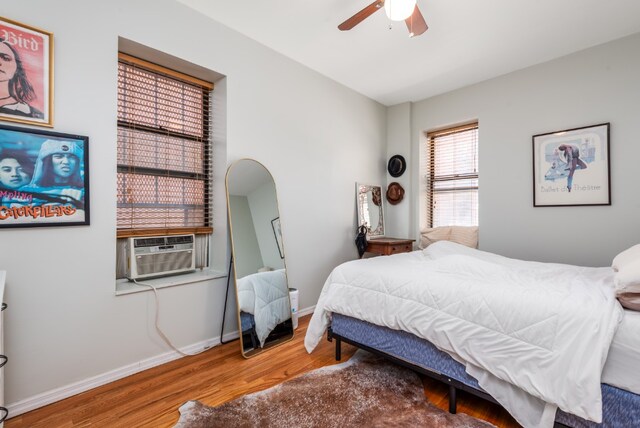 bedroom with arched walkways, a ceiling fan, wood finished floors, cooling unit, and baseboards