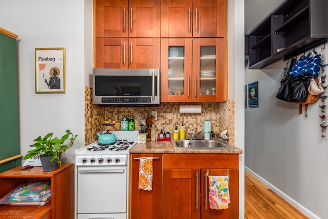 kitchen featuring tasteful backsplash, light countertops, stainless steel microwave, glass insert cabinets, and white range with gas stovetop