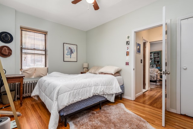 bedroom featuring a ceiling fan, radiator, baseboards, and wood finished floors