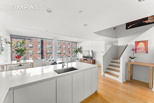 kitchen with white cabinetry, light wood-style floors, open floor plan, and a sink