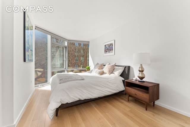 bedroom featuring hardwood / wood-style flooring, expansive windows, and baseboards