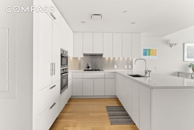 kitchen with gas cooktop, a peninsula, a sink, light wood-style floors, and decorative backsplash