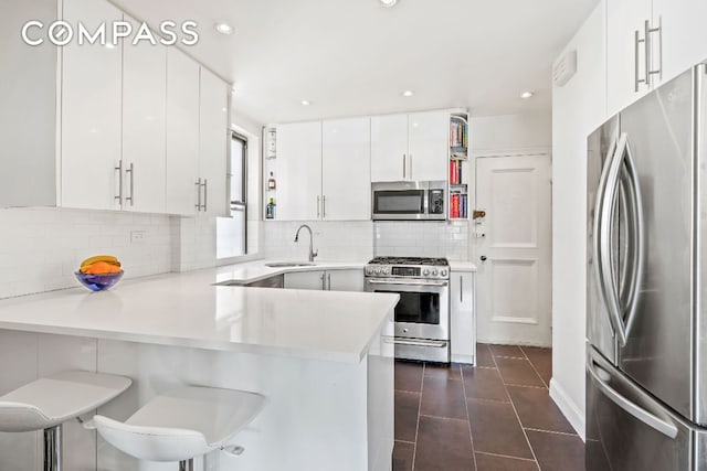 kitchen featuring sink, appliances with stainless steel finishes, a kitchen breakfast bar, white cabinets, and kitchen peninsula