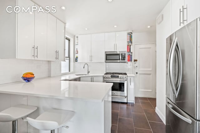 kitchen with a breakfast bar area, stainless steel appliances, light countertops, white cabinets, and a peninsula