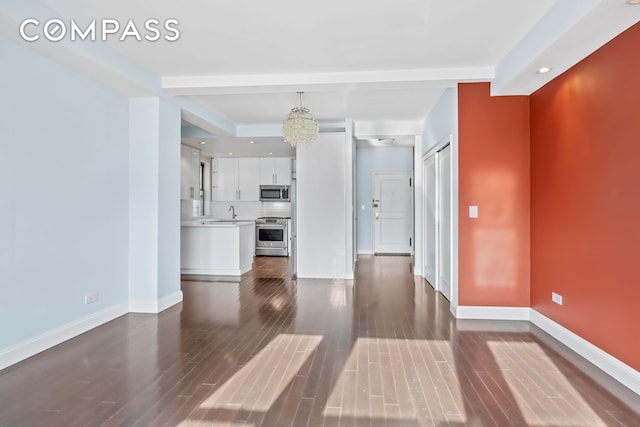 unfurnished living room featuring baseboards, dark wood-style flooring, an inviting chandelier, a sink, and recessed lighting