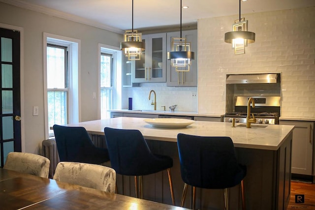 kitchen with extractor fan, a center island with sink, a kitchen bar, hanging light fixtures, and stainless steel range