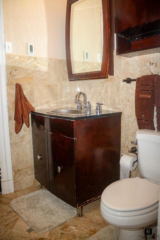 bathroom with toilet, vanity, and tile walls