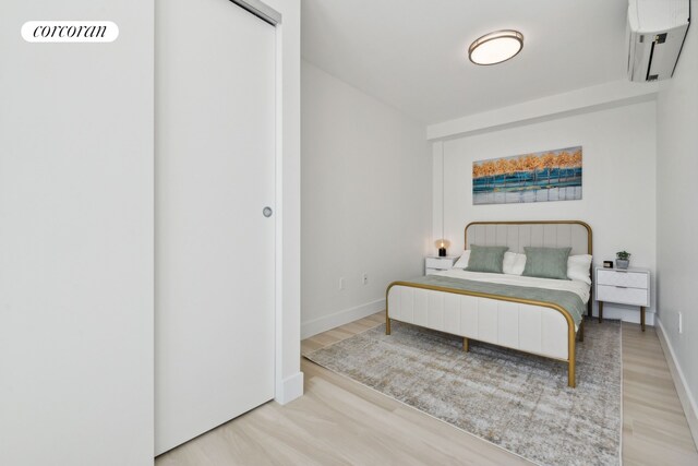 bedroom with a wall mounted AC, wood finished floors, and baseboards