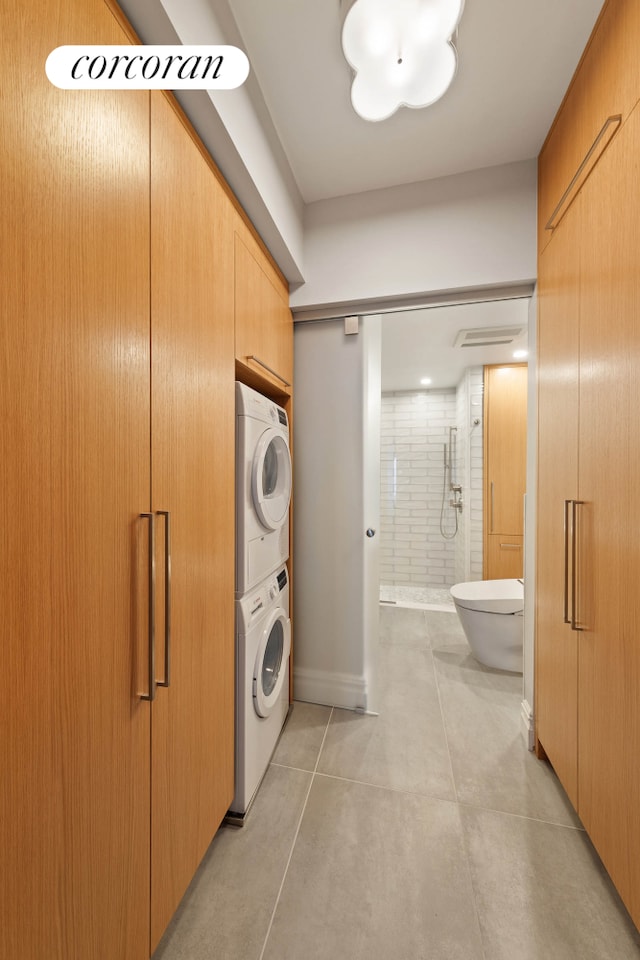 laundry area featuring light tile patterned floors, stacked washer and dryer, laundry area, and baseboards