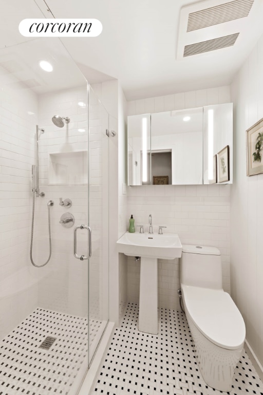 bathroom featuring toilet, backsplash, tile walls, walk in shower, and sink