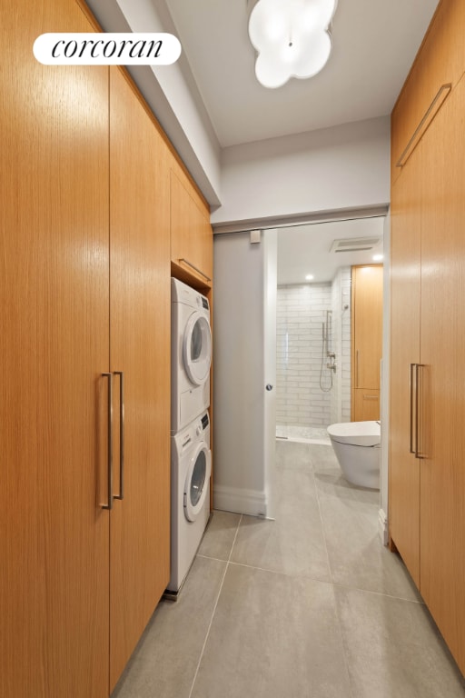 laundry room featuring stacked washer / drying machine and light tile patterned floors