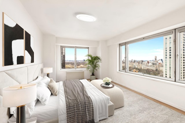 bedroom with wood finished floors, multiple windows, baseboards, and a city view