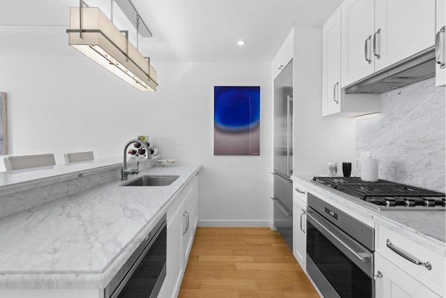 kitchen with appliances with stainless steel finishes, white cabinets, light stone counters, and sink