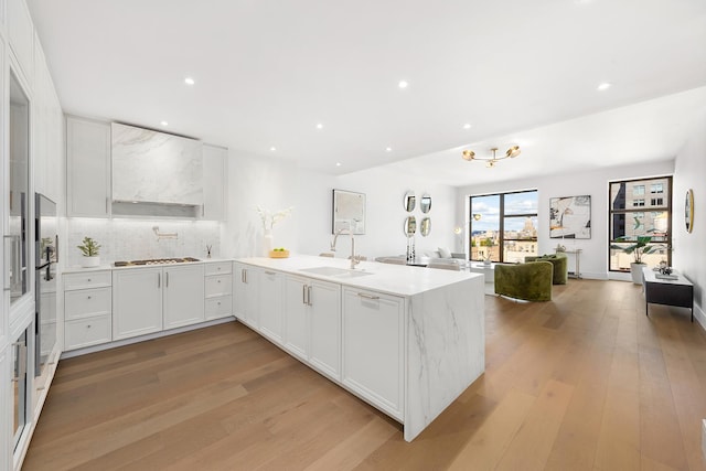 kitchen with stainless steel gas cooktop, a sink, white cabinetry, light wood-style floors, and open floor plan