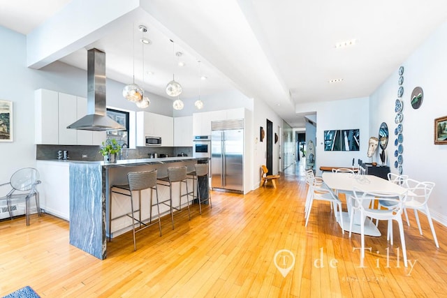 kitchen with stainless steel appliances, decorative backsplash, island range hood, and white cabinetry