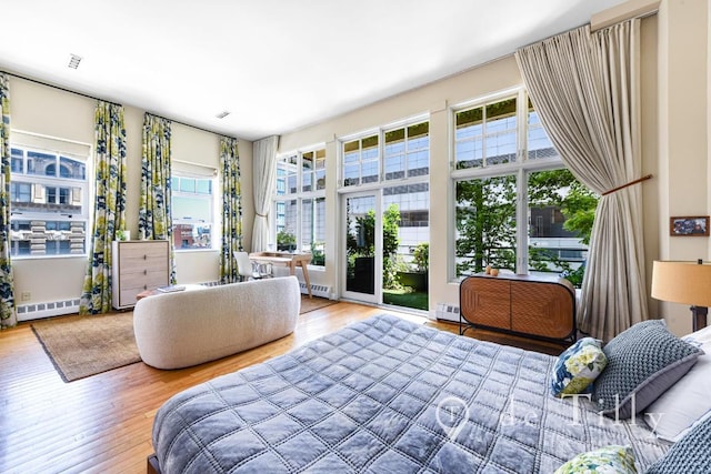 bedroom with wood-type flooring, multiple windows, and a baseboard radiator