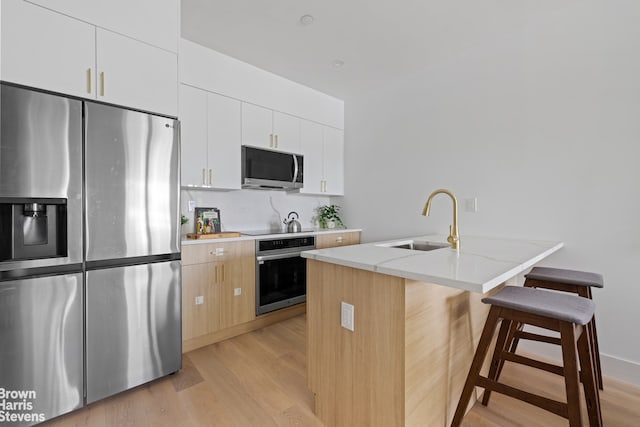 kitchen with a kitchen island with sink, stainless steel appliances, a sink, white cabinets, and a kitchen breakfast bar