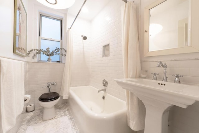 bathroom with tile walls, shower / bathtub combination with curtain, toilet, a sink, and tile patterned flooring