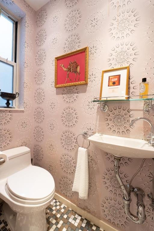 half bathroom featuring baseboards, a sink, toilet, and wallpapered walls