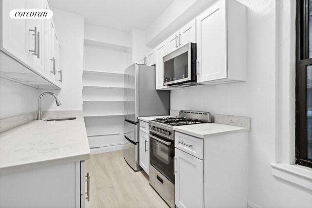 kitchen featuring appliances with stainless steel finishes, light wood-type flooring, light stone countertops, white cabinets, and sink