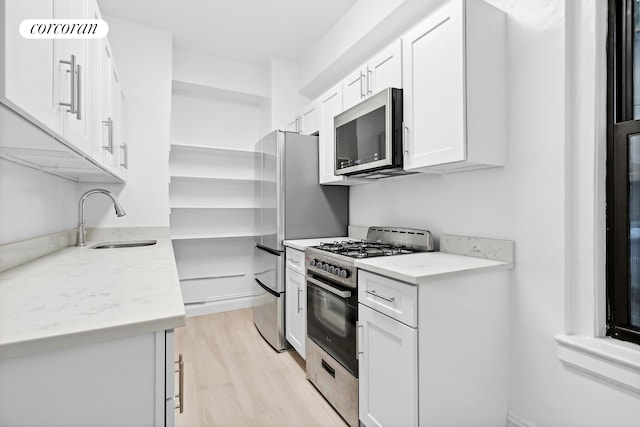 141 E 3rd St Unit 6B, New York City, NY 10009 - kitchen featuring appliances with stainless steel finishes, a sink, white cabinets, light wood finished floors, and light stone counters