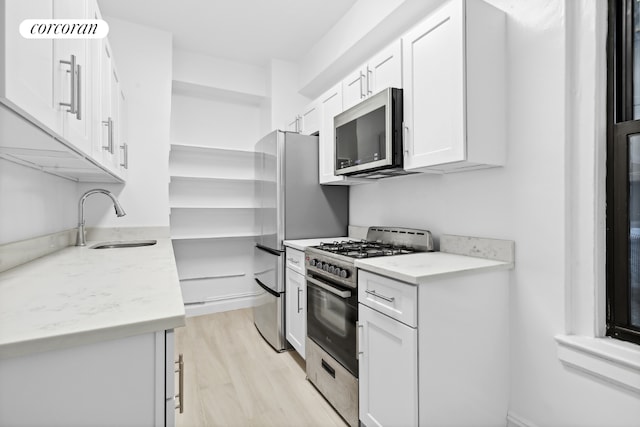 kitchen featuring light stone counters, stainless steel appliances, a sink, white cabinets, and open shelves