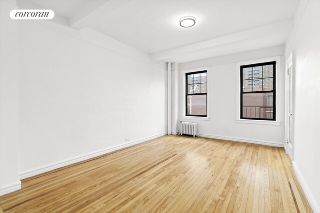 spare room featuring light wood finished floors, baseboards, visible vents, radiator, and beam ceiling