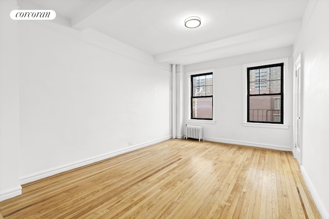 spare room featuring radiator, light wood-style flooring, baseboards, and beam ceiling
