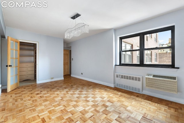 unfurnished bedroom featuring light parquet floors, a chandelier, a wall mounted AC, and radiator heating unit