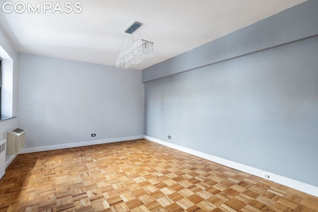 empty room featuring light parquet floors, a notable chandelier, and a wall mounted air conditioner