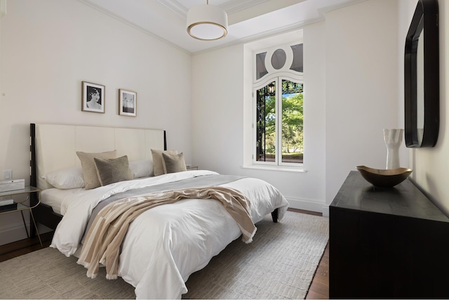 bedroom with ornamental molding, a tray ceiling, baseboards, and wood finished floors