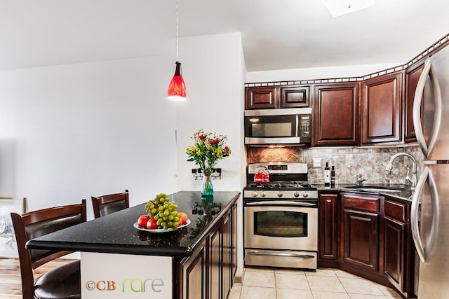 kitchen featuring appliances with stainless steel finishes, a breakfast bar, a sink, a peninsula, and backsplash