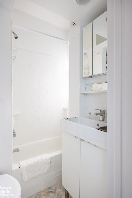 full bathroom with parquet floors, decorative backsplash, tiled shower / bath combo, vanity, and toilet