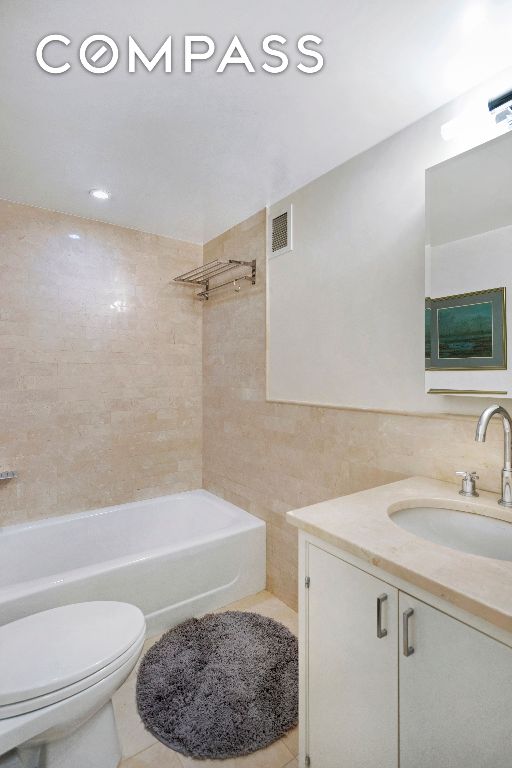 full bathroom with tiled shower / bath, toilet, tile walls, tile patterned floors, and vanity