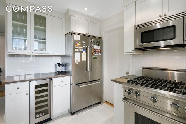 kitchen with stainless steel appliances, white cabinetry, beverage cooler, and backsplash