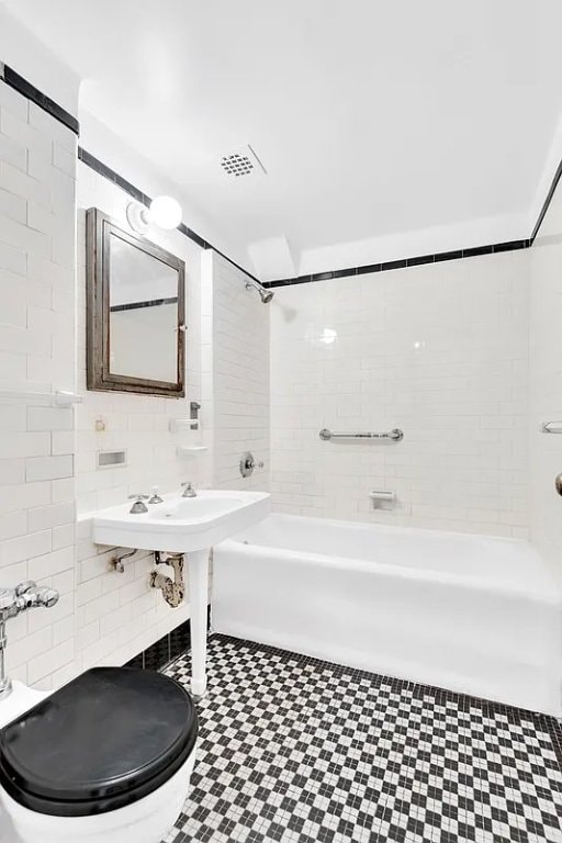 bathroom with toilet, tiled shower / bath, and tile walls