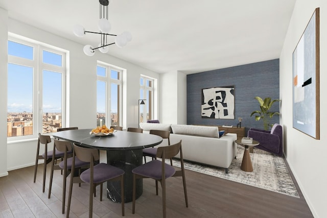 dining space with an accent wall, a notable chandelier, baseboards, and wood finished floors