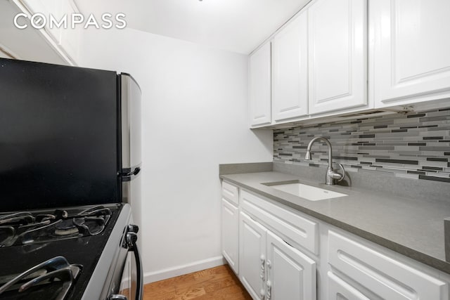 kitchen with stainless steel appliances, a sink, light wood-style floors, white cabinets, and decorative backsplash