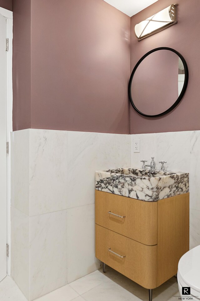 half bath with toilet, tile walls, wainscoting, and vanity